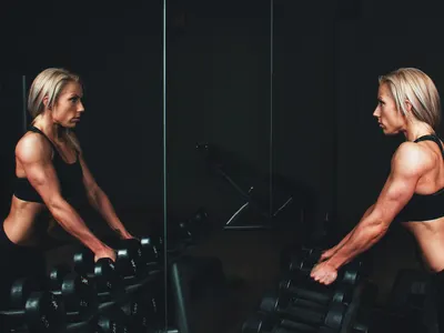Woman lifting dumbbells in front of a mirror